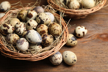 Obraz premium Wicker bowls, quail eggs and straw on wooden table, closeup. Space for text