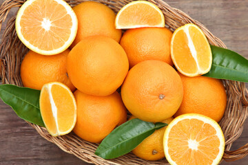 Wicker basket with ripe juicy oranges and green leaves on wooden table, top view