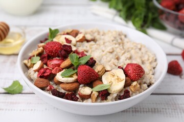 Delicious oatmeal with freeze dried berries, banana, nuts and mint on white wooden table, closeup