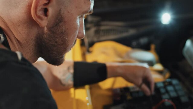 Over shoulder close up of auto mechanic connecting wires in engine under motor hood, tattoo on his right arm