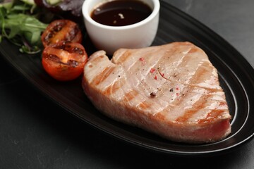 Delicious tuna steak, tomato and sauce on black table, closeup