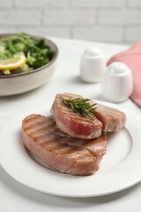 Delicious tuna steaks with rosemary on white table, closeup