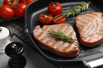 Delicious tuna steaks with rosemary and tomatoes on grey table, closeup