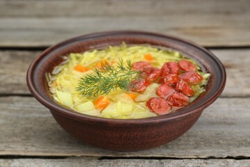 Bowl of delicious sauerkraut soup with smoked sausages and dill on wooden table
