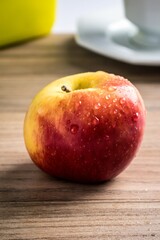 an apple on a table with water droplets on it, next to coffee cup
