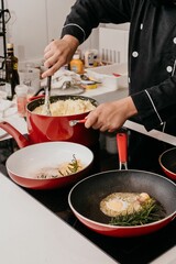 chef adding finishing ingredients into pans on stove in kitchen