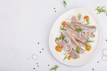 Salted herring with dijon mustard, dill and red onion rings. Marinated filleted fish on light stone