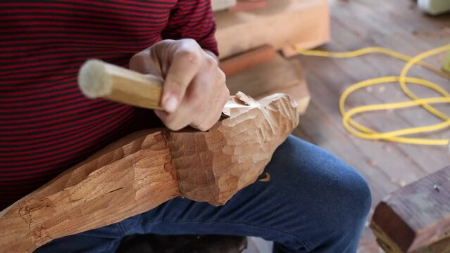 Artisan man using a hummer and a knife carving wooden holy statue