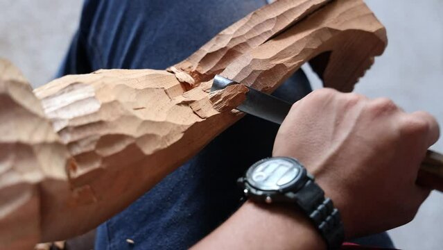 Artisan man using a knife to carve a wooden holy statue at a workshop