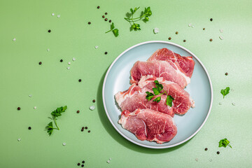 Pieces of pork meat with parsley on gray dish, raw fresh steaks concept. Sea salt, spices