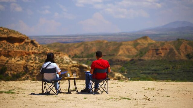 Men sitting on chairs against semi desert landscapes in windy weather in Spain