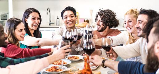 Friends toasting red wine glasses at dinner while eating spaghetti with tomato - Multiethnic guys having fun together at dinner with italian pasta and red wine - Banner or header with bright filter