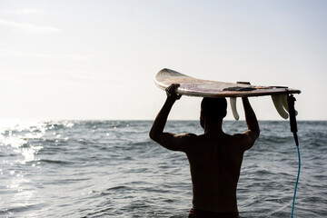 Surfer holding his surfboard on the head - Hipster man standing on the beach and waiting big waves for surfing - Fit bearded man training with surfboard to sea - Lifestyle and freedom concept