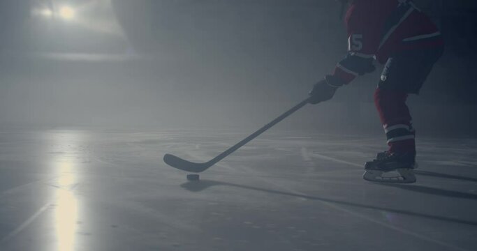 Hockey player in red uniform skating on ice stick handling puck in the dark