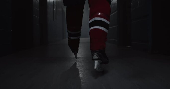 Hockey player in red uniform walking down dark hallway in arena