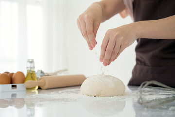 Cook hands kneading dough, sprinkling piece of dough with white  flour. Low key shot, close up on hands, some ingredients around on table.