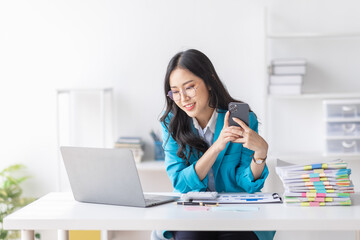 Business Asian woman hold phone and use laptop at the workplace. Project stats financial data sales charts on laptop and cellphone Asian finance concept
