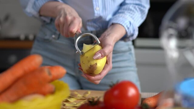Housewife cooking vegetables for lunch. Female person peeling off potatoes with a modern peeler tool
