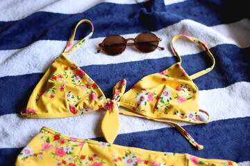 Striped beach towel, floral yellow swimsuit, sunglasses and mesh bag with peaches. Cute beach essentials. Selective focus.