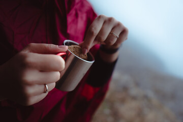 A woman eating a cookie on a hiking with a cup of tea