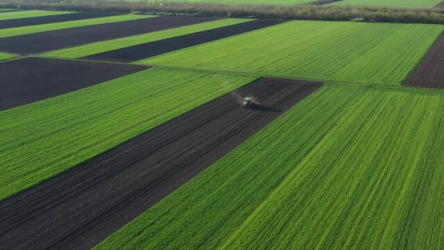 Above rotation view, orbit dolly move, of tractor as pulling mechanical seeder machine over arable field, soil, planting new cereal crop, corn, maize.