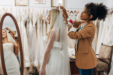An assistant is putting a veil on a happy brides head