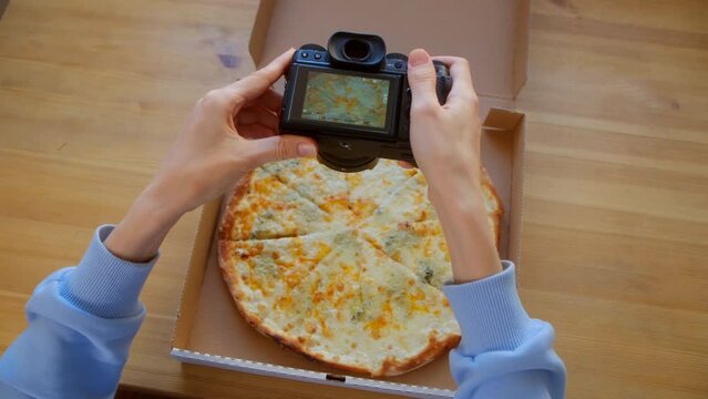 Top view - Female hands use digital camera photographing appetizing fresh cooked italian Quattro Formaggi Pizza on wooden background. Food blog of blogging. Technology, food porn concept.