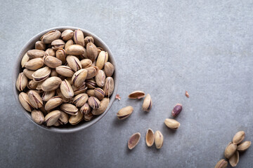 Bowl with pistachios on a grey concrete background. Green salted pistachios in a ceramic bowl. Copy space.