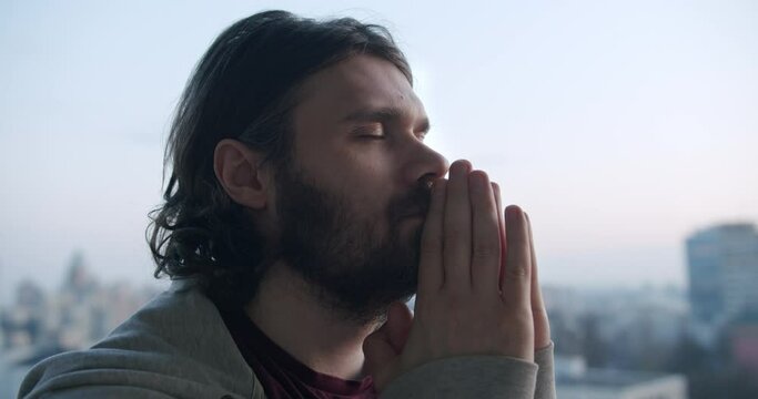 Prayer man troubled with personal problem and asking for help. Eyes closed, hands together to praying with hope. Faith with folded hands pray. Strong faith and Christian beliefs concept. Urban city