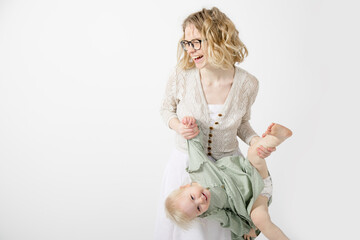 Portrait of happy family posing on white background. Young joyful woman mother holding leg, hand of little blond girl.