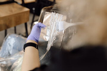 Unrecognizable woman hairstylist colorist hold strand of long hair on foil, applying hair color...