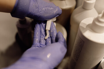 Cropped photo of woman hairdresser wearing blue rubber gloves, squeezing out shampoo mask...