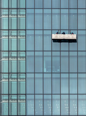 A glass building wall with window washers descending the facade on a lift platform in Tokyo, Japan