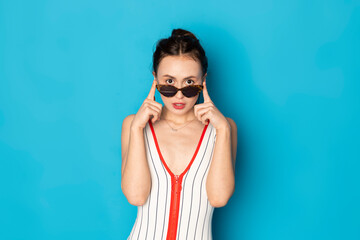 Beautiful happy young woman posing in a sensual white striped swimsuit. Isolated on blue background.