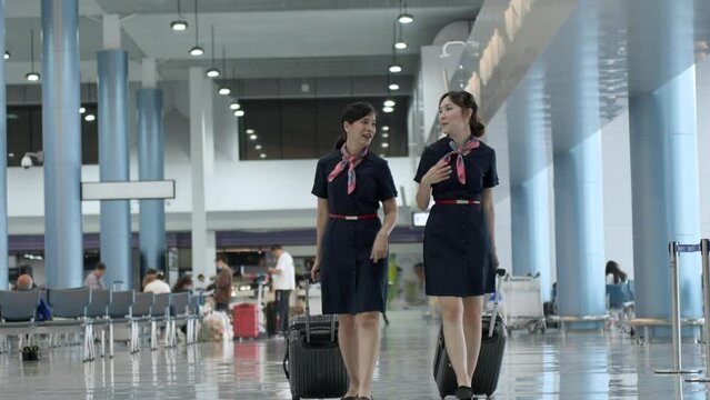 Beautiful asian cabin crew women dragging wheeled luggage in terminal to work at airport , Job and occupation airline workers concept.