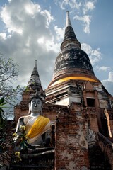 Vertical shot of the statue of Buddha in front of two pagodas in Ayutthaya, Thailand.
