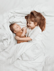 Little sister hugging her newborn baby. Toddler kid meeting new sibling. Cute boy and new born baby boy relax in a white bedroom. Family with children at home. Love, trust and tenderness