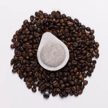Coffee paper pod dosette for espresso laying on fresh ground coffee beans. Isolated on white background. Compostable, disposable coffee filter for sustainable living