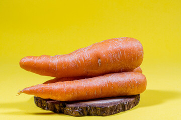 Carrots on sliced wooden log, on a yellow background