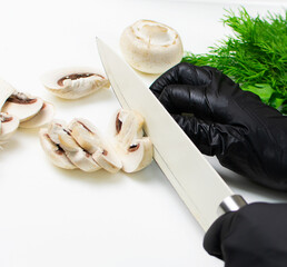 Hands of cook in black rubber gloves cut mushrooms with knife