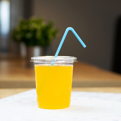 Plastic cup with orange drink and straw on table in cafe
