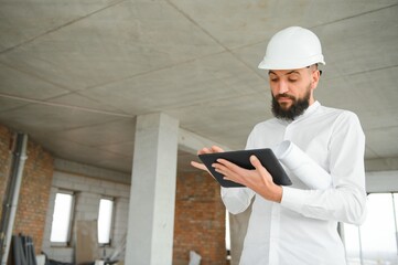 Serious busy young attractive arabic industrial engineer in hard hat with project drawings in...