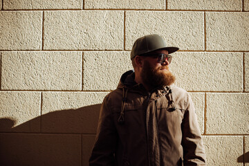Portrait of handsome bearded ginger man with sunglasses and green baseball flat cap, against yellow...
