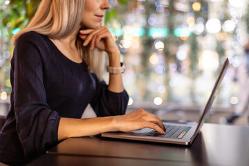Cropped image of woman sitting at cafe with laptop. Blond hair lady working with notebook at home or cafeteria. Freelance, work from home and distant work concept.