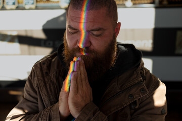 Portrait of bearded man praying, with a glare of light in the form of a rainbow on his face - a...