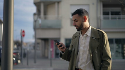 One Middle Eastern young man standing in city street checking phone. An Arab male person looking at online content outside