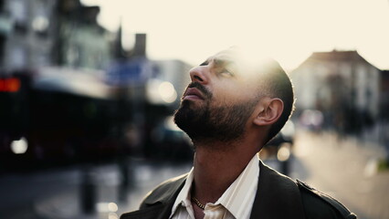 One meditative young Arab man standing in street looking at Sky having a spiritual experience. Close-up face of a Middle Eastern Male person stands outdoors in urban environment in tracking shot