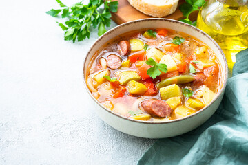 Minestrone soup, italian vegetable soup with smoked sausages, Top view on white table.