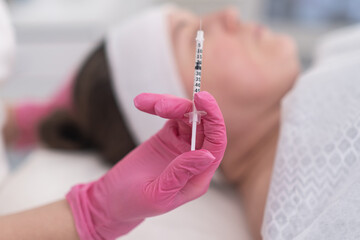 Professional beautician holding syringe to smoothing wrinkles with injections. woman lies relaxed with her eyes closed in a modern beauty salon. 