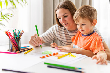 Mother and child drawing with pencils sitting at the desk at home